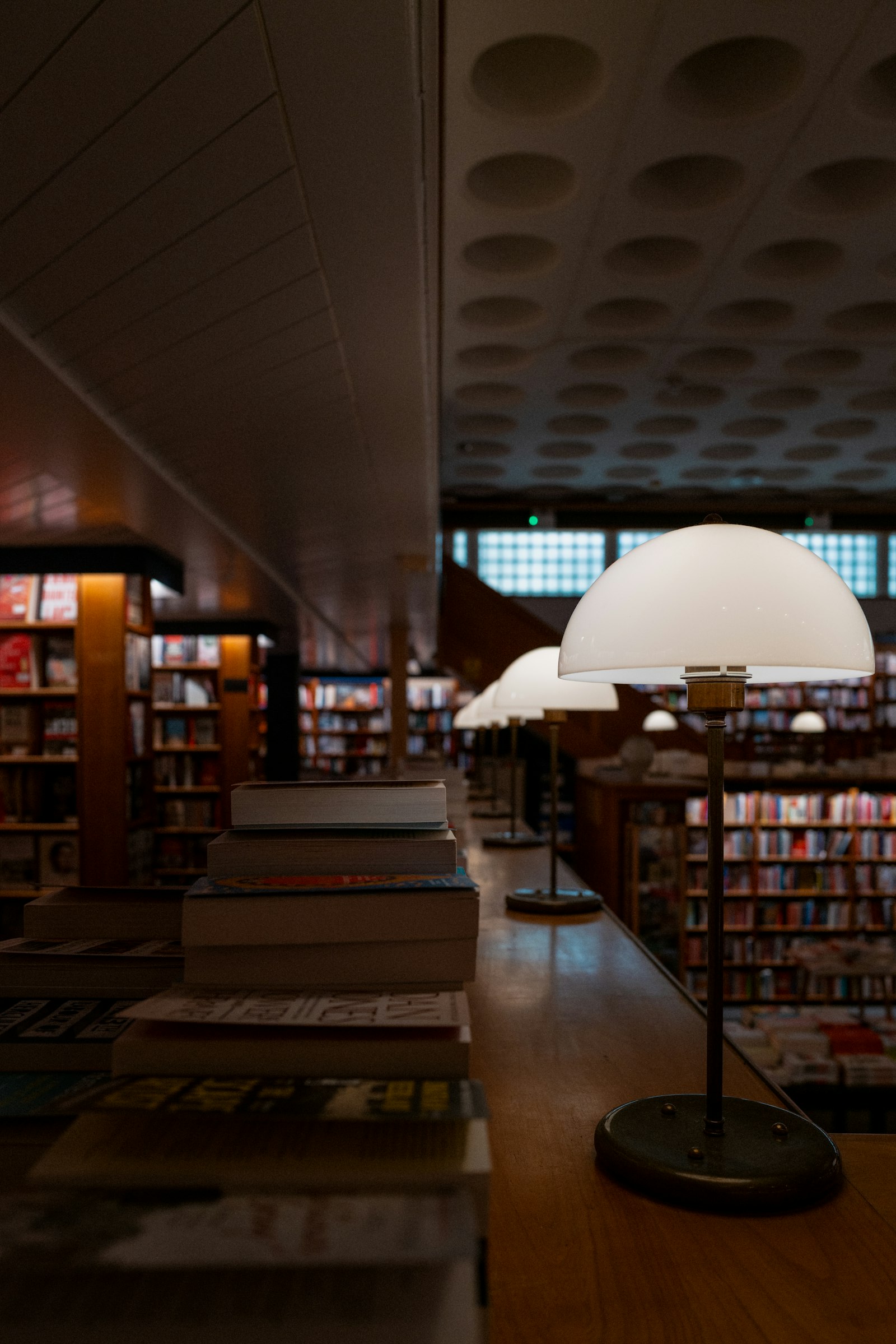 A warm library reading room lined with books, lit by brass lamps